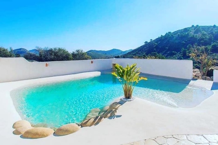 Piscina de arena estilo natural con formas orgánicas y acabado blanco integrada en entorno mediterráneo, proyecto de Paradise Pools Spain especializado en diseño y construcción de piscinas en Valencia